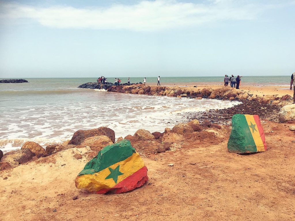 Beach in Saly, Senegal. Senegalese flag painted in two stones. Participants of the francophone forum on the background. 