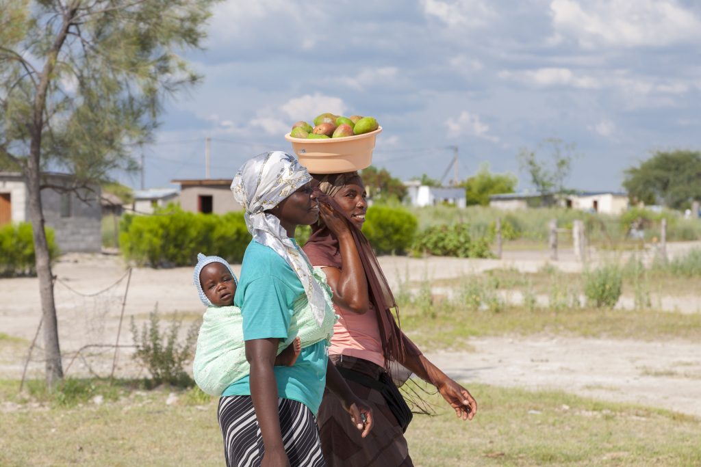 : Retrato de hermosas mujeres negras africanas caminando con velo, pueblo tradicional en el fondo. Botsuana 2019