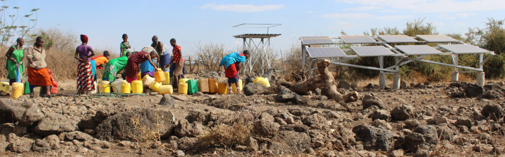 Des femmes au Kenya vont chercher de l'eau à côté de panneaux solaires.
