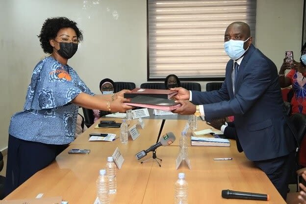 Two ministry workers exchange signature books across a table.