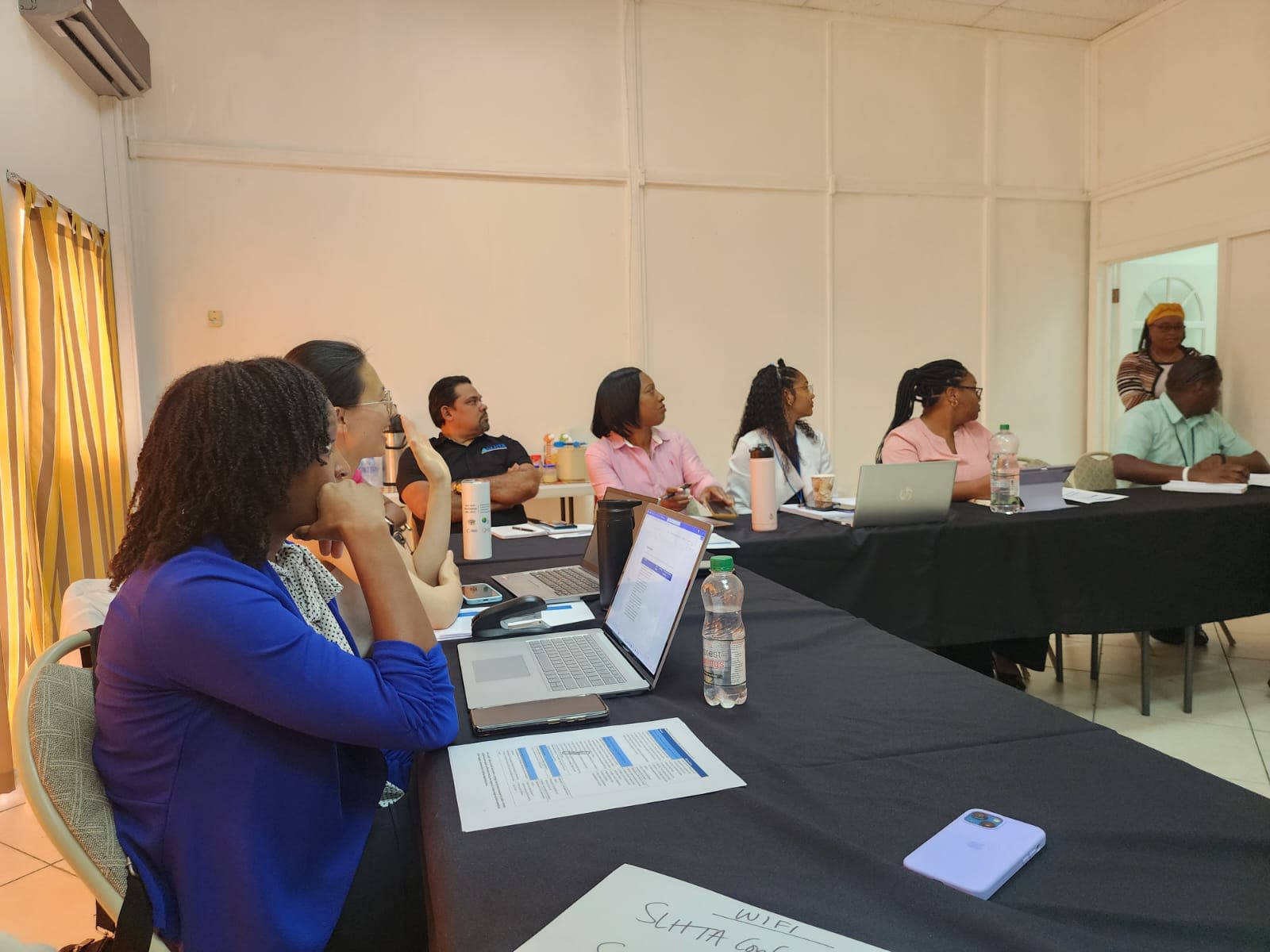 Participants seated around a long table in a room, attending a focus group or meeting, with laptops and papers visible.
