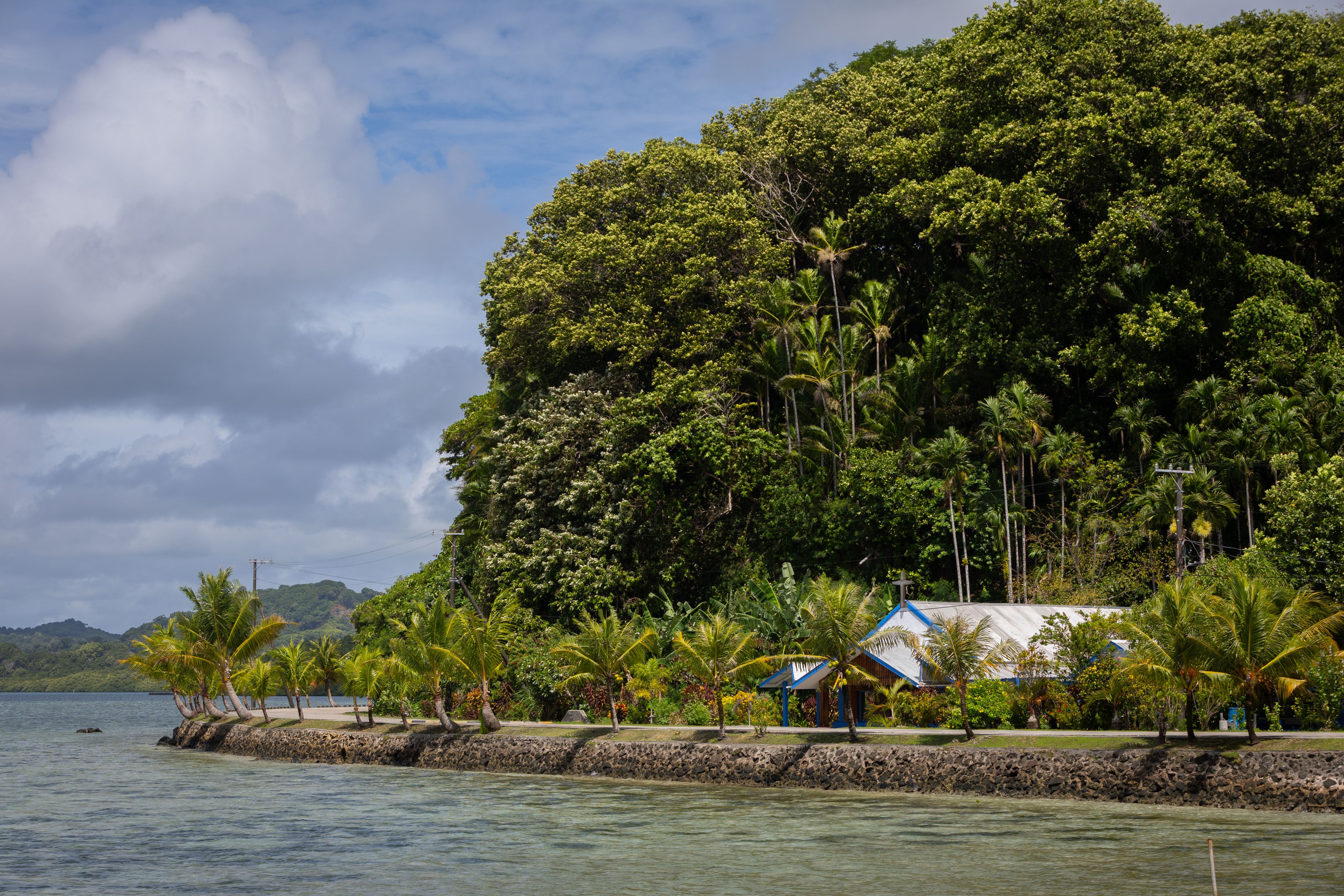 A small white building near a road close to shore. 