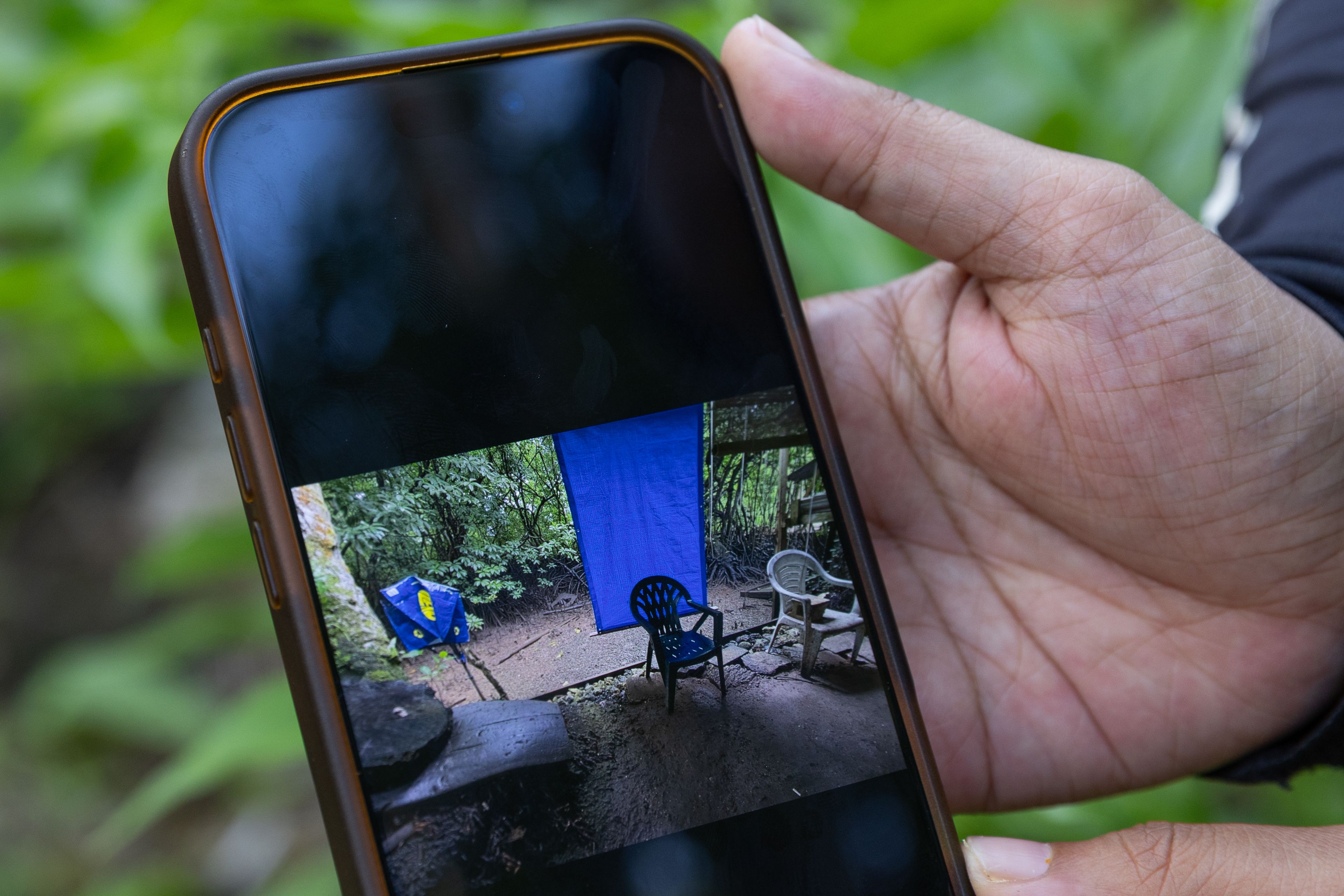 A hand holding a phone with an image of a backyard on the screen. 
