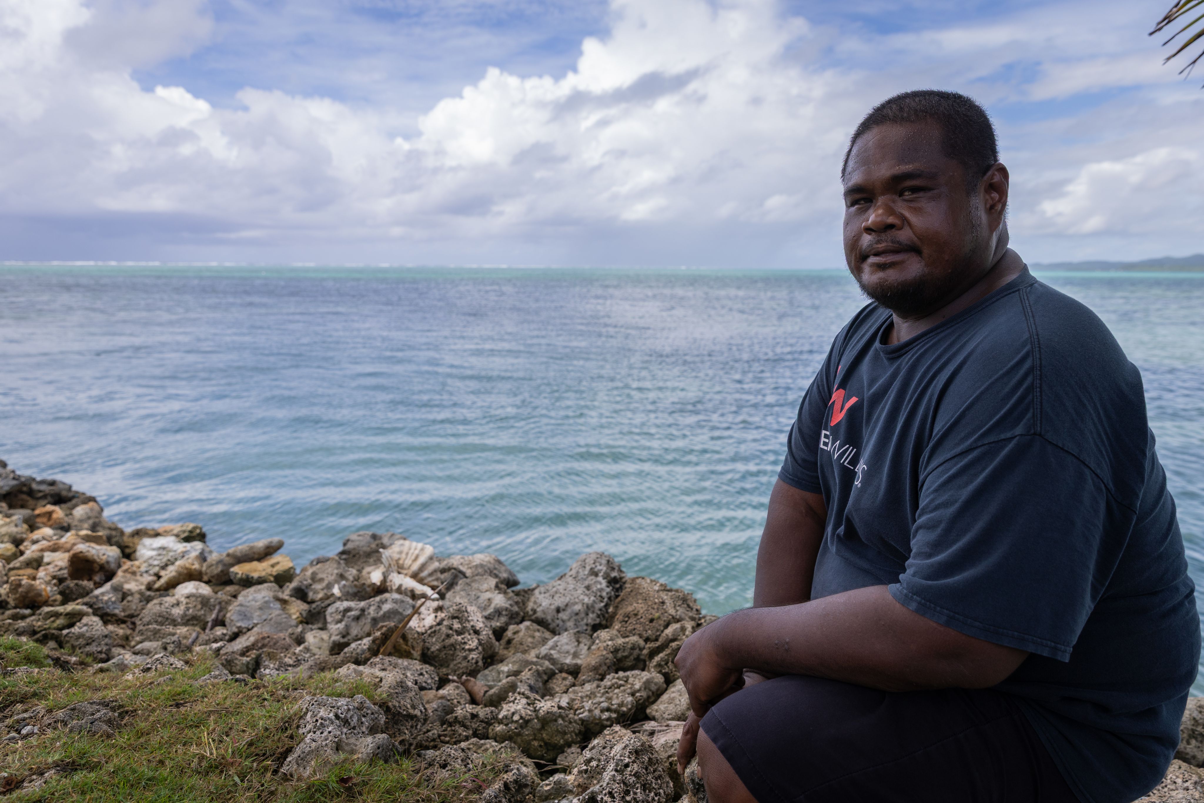 A man sits by a sea wall with the ocean in the background. 