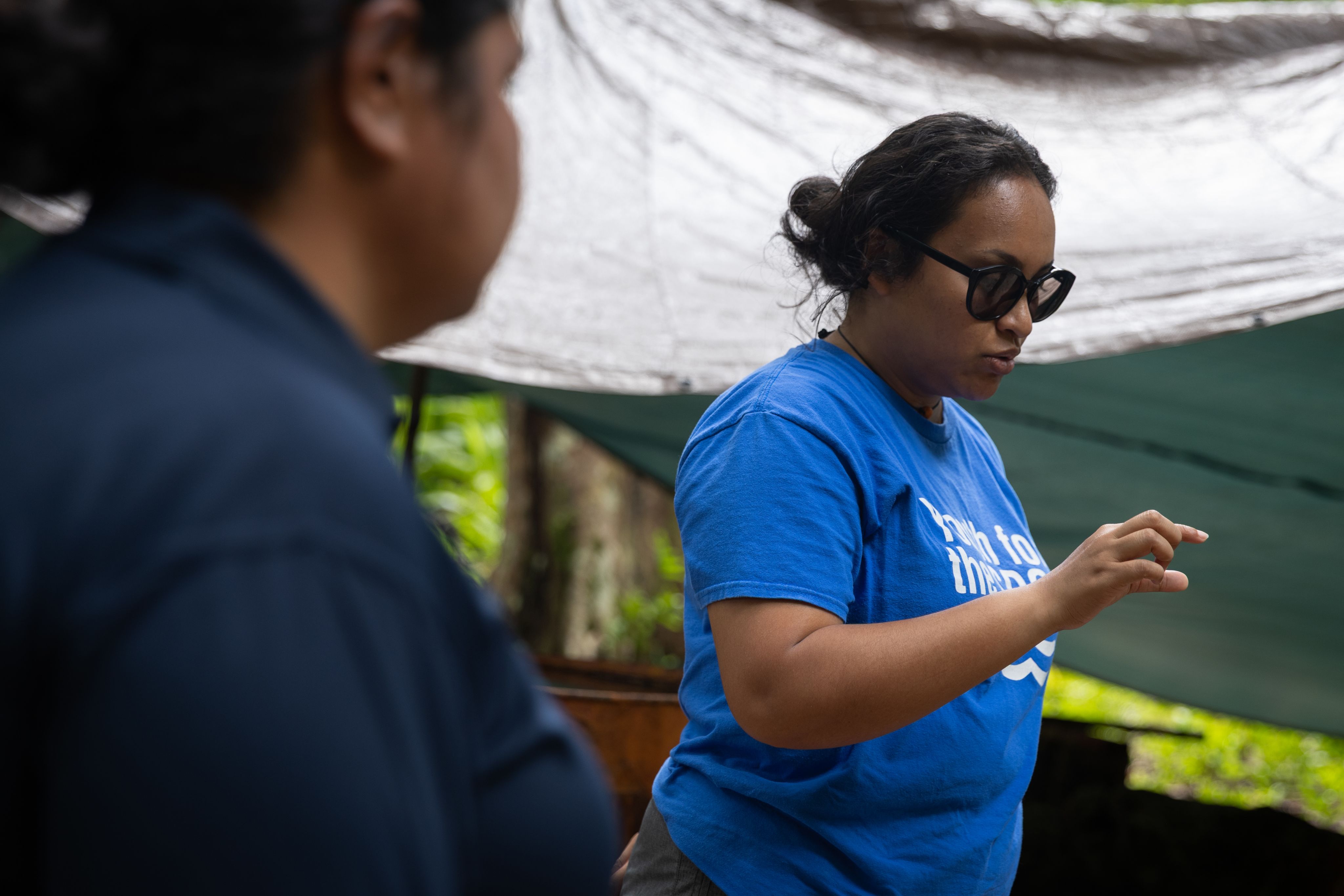 A woman wearing black sunglasses and a blue t-shirt.